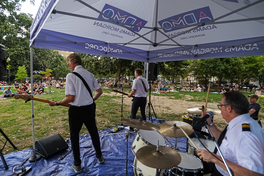 A band performs under a tent at an outdoor event as a crowd enjoys the show in a park in Washington, DC.